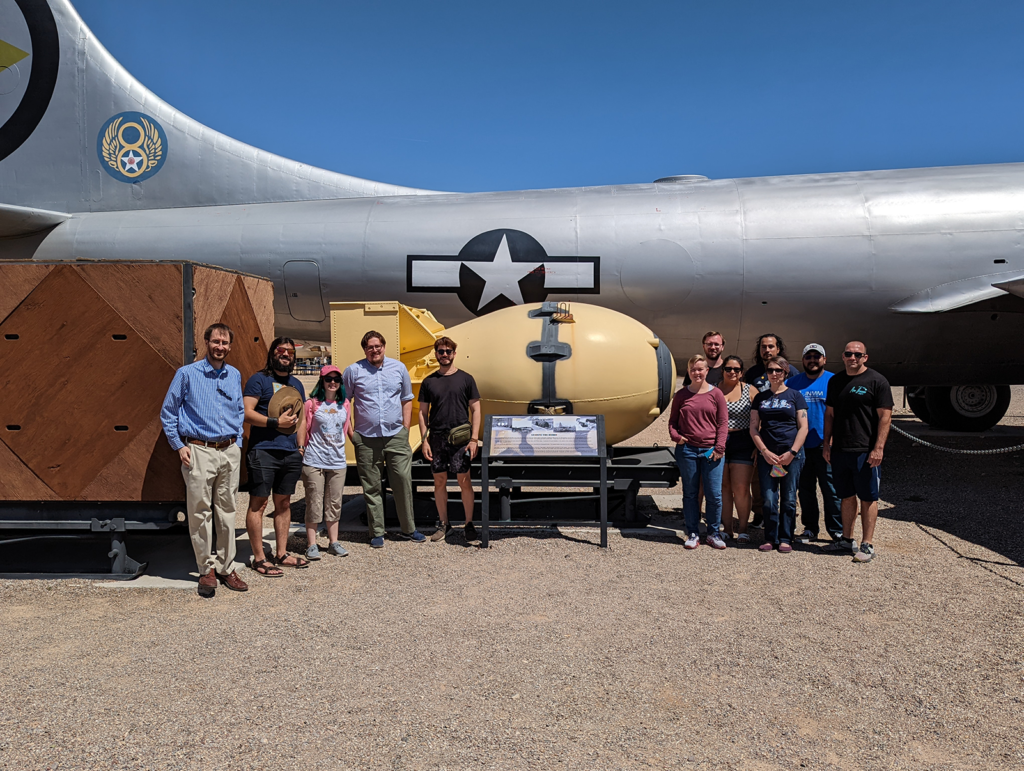 group pictured in front of WWII era bomber and atom bomb model.